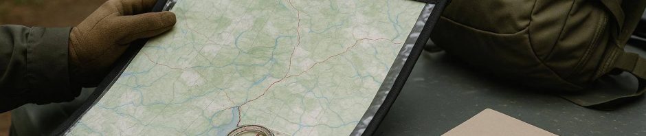 A paper access map, compass, notebook, and muddy hunting boots beside a closed rural gate